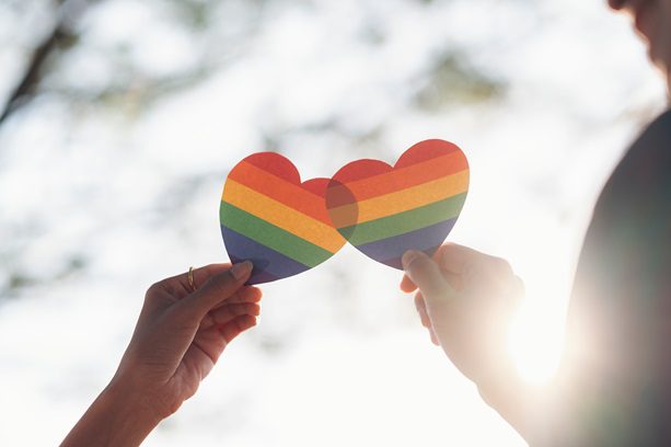 A family shares their joy with two rainbow colored hearts held up to the sunshine.